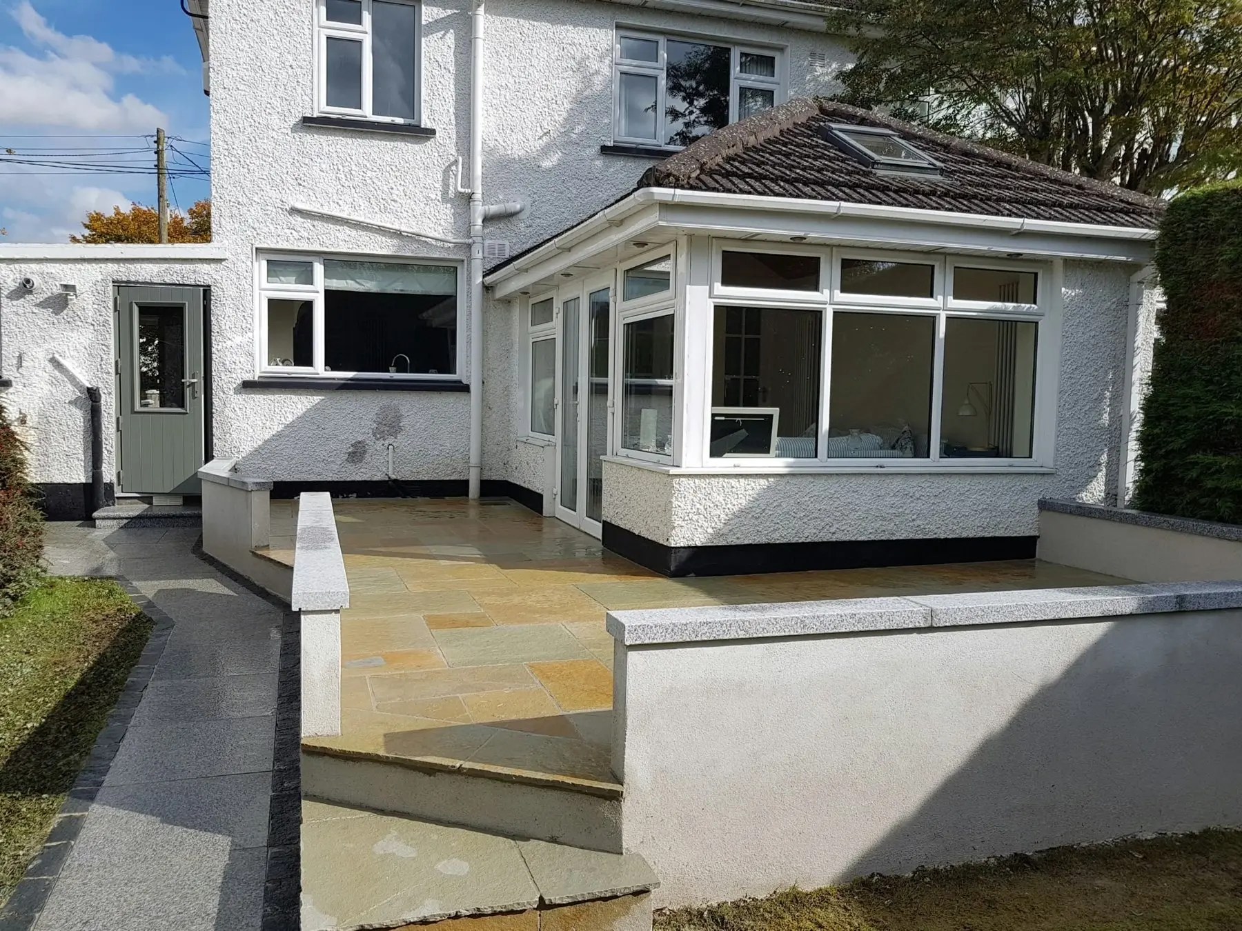The same garden after landscaping — new sandstone patio with rendered seating walls beside the conservatory