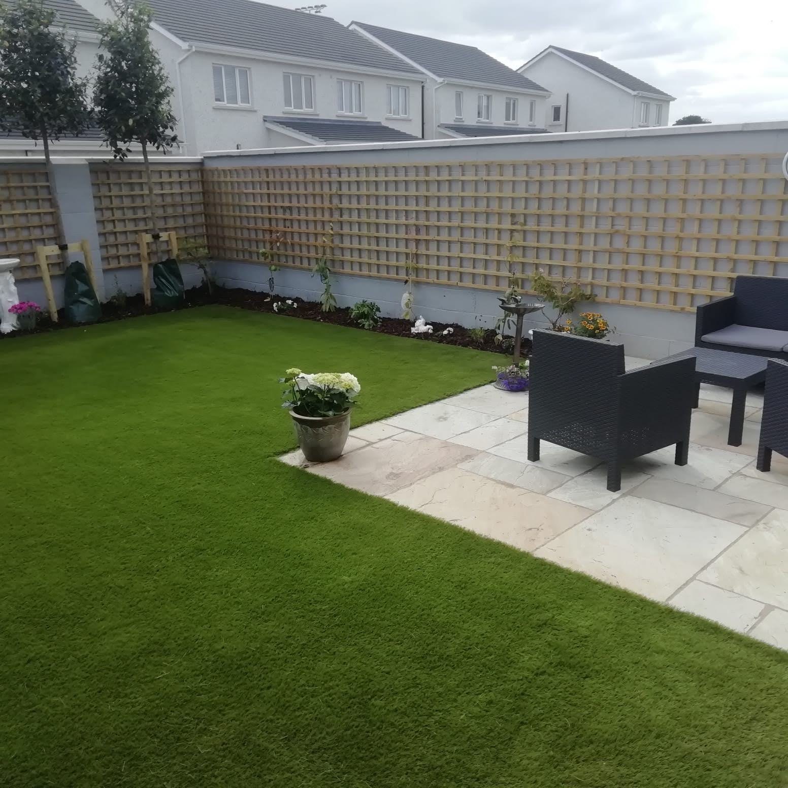The same back garden after landscaping — fresh lawn, timber screening, planting and a paved seating area