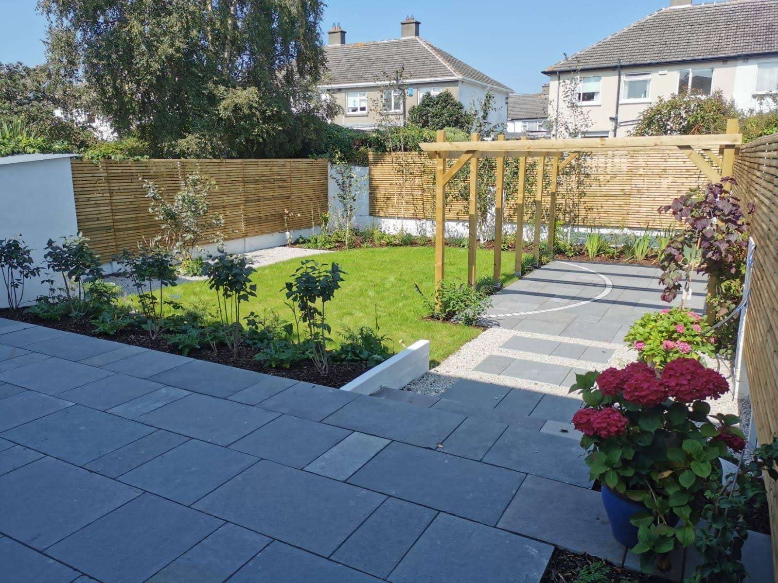 The same back garden after landscaping — timber screens, new lawn, planting beds, gravel and a timber pergola