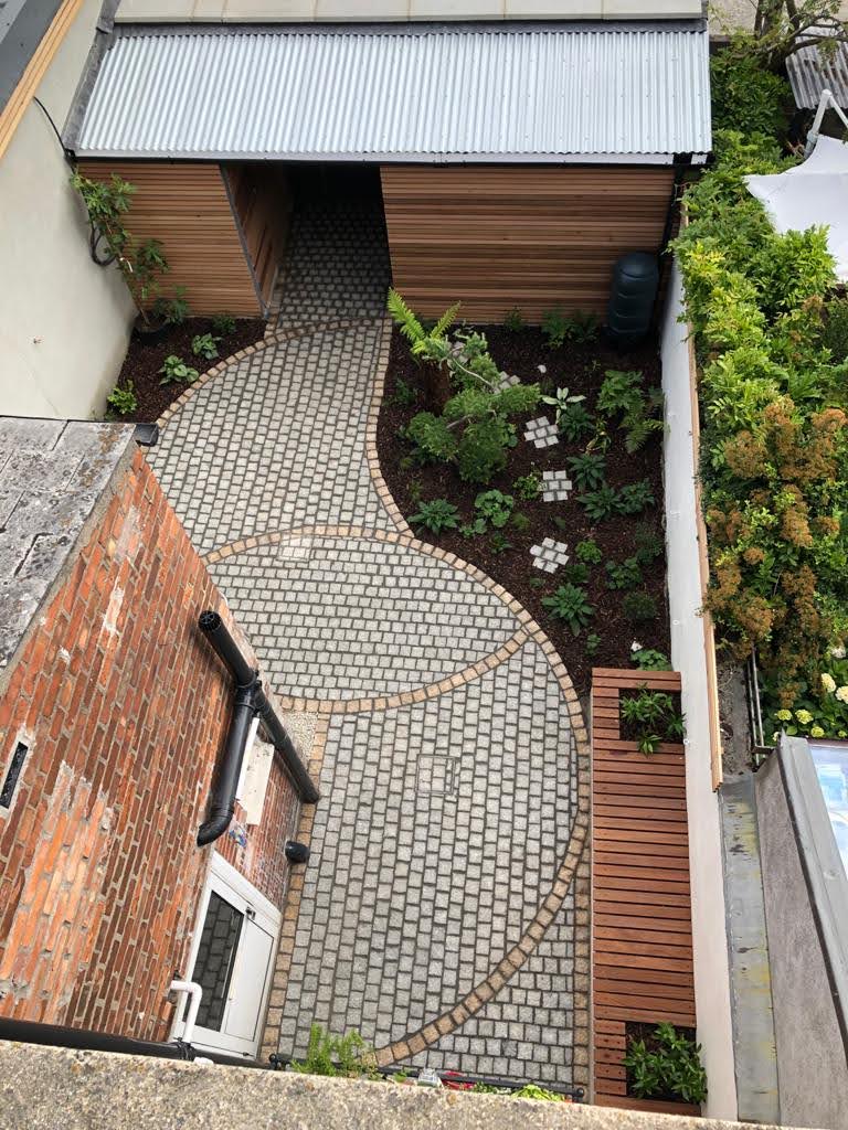 The same rear yard after landscaping — curved granite setts, mulched planting beds, a slatted timber bench and new timber screening